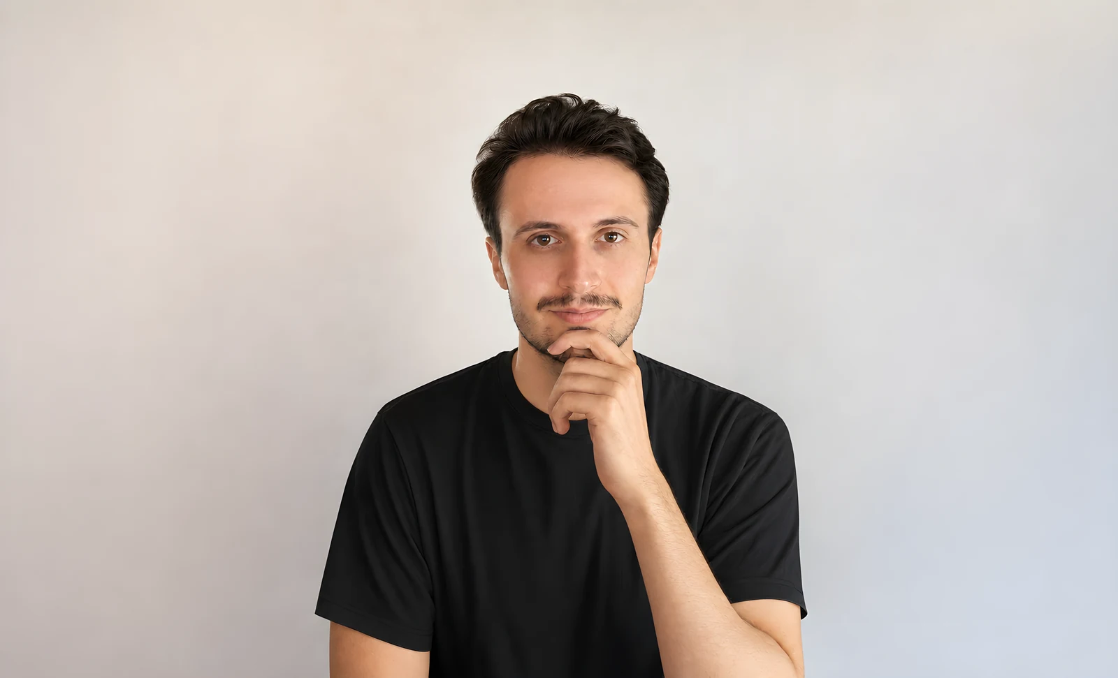 Portrait of Julian Juelich, resting his chin on his hand, against a plain light grey background.
