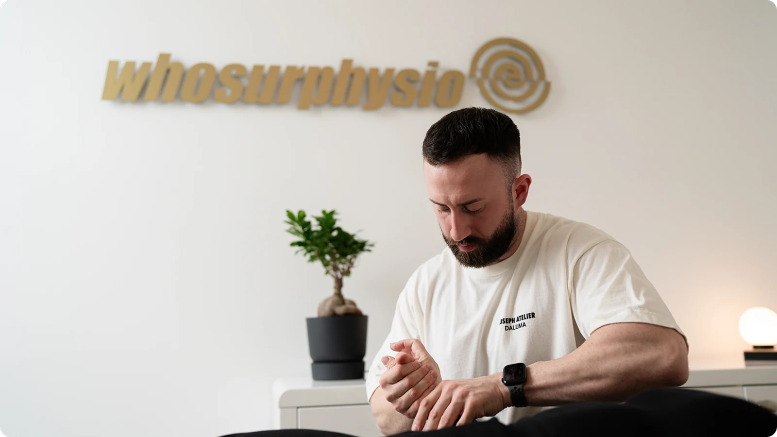 Julian Klug in his practice in Frankfurt, the whosurphysio logo on the wall behind him.